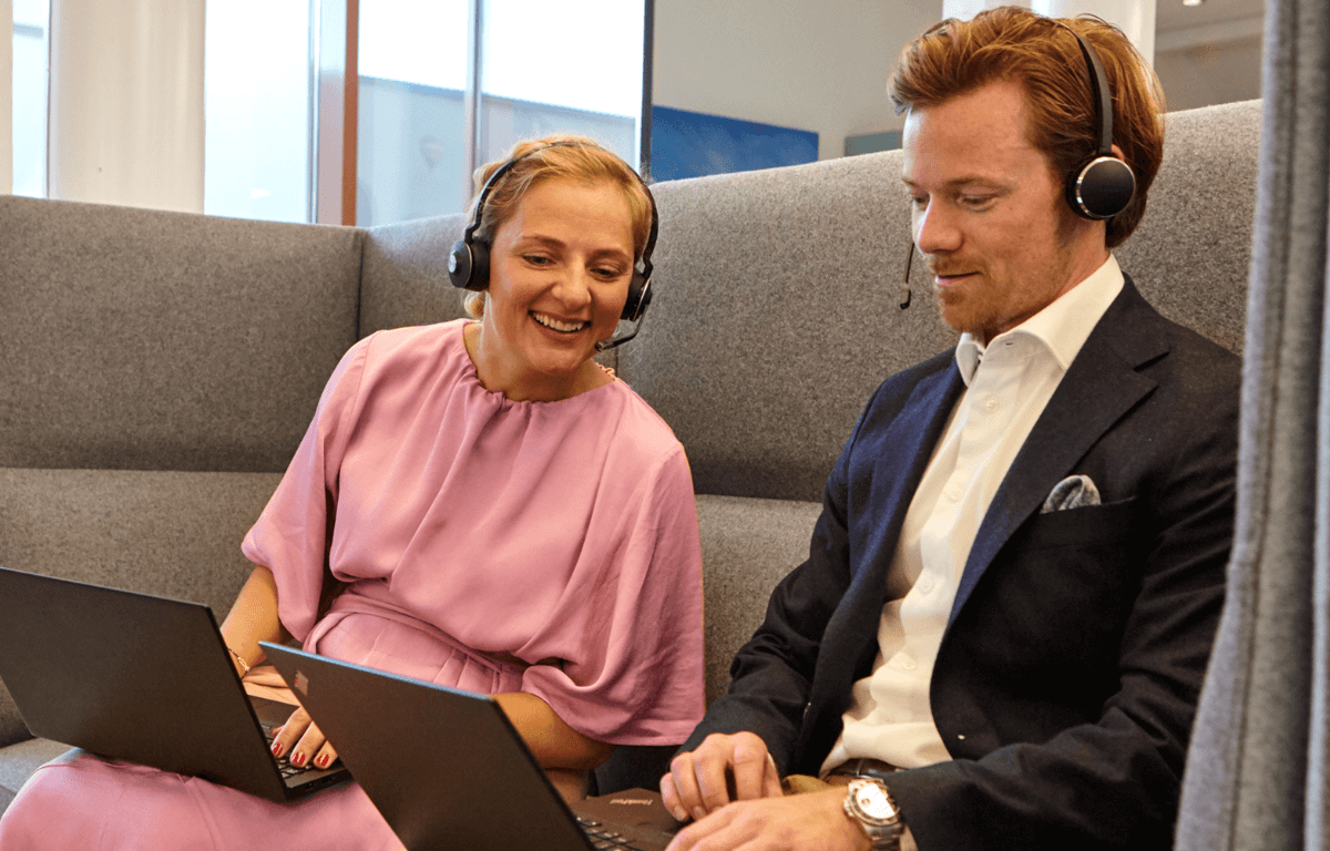 Colleagues with head phones sitting in a sofa looking at a screen